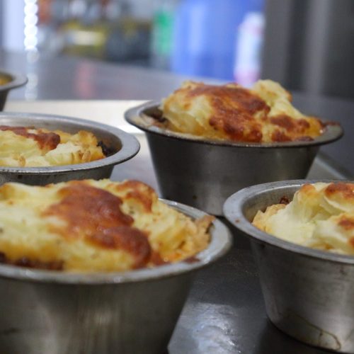 Close-Up Of Five Individual Shepherd’S Pies In Metal Baking Dishes On A Metal Surface. The Classic Pies, With Their Golden-Brown, Crispy Mashed Potato Tops, Evoke The Essence Of Comfort Food In An Industrial Kitchen Environment, Reminiscent Of Scenes From A Professional Cooking Program. Close-Up Of Five Individual Shepherd'S Pies In Metal Baking Dishes On A Metal Surface. The Classic Pies, With Their Golden-Brown, Crispy Mashed Potato Tops, Evoke The Essence Of Comfort Food In An Industrial Kitchen Environment, Reminiscent Of Scenes From A Professional Cooking Program.